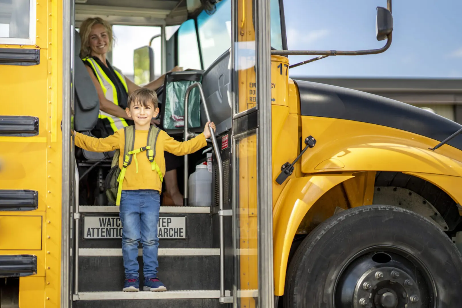 Child boarding yellow school bus, driver smiling.